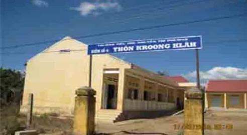 A single-story building with a sign on the roof stating "Nha Tho Khrong Klan." The structure is surrounded by a grassy area, and there is a clear blue sky above.