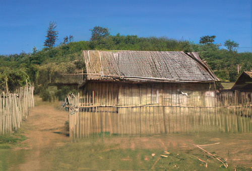 A small bamboo hut with a metal roof is surrounded by a simple wooden fence. There is a dirt path leading to the hut, and trees can be seen in the background under a clear blue sky.