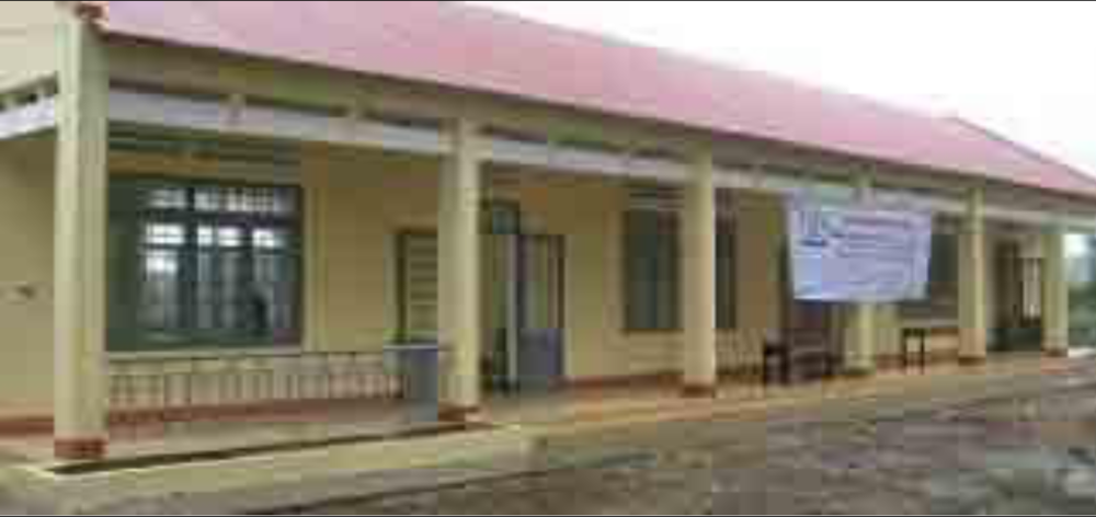 A single-story building with a red roof and a light yellow exterior. A large sign is attached to the front, and there is a small veranda with pillars at the entrance.