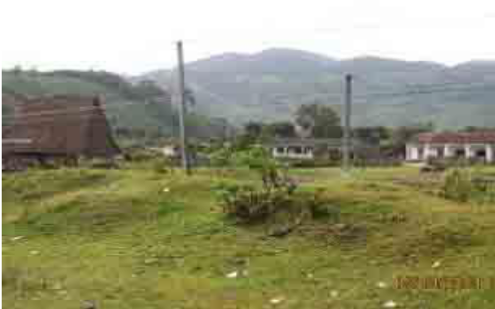 A row of single-story buildings with a few people sitting and standing outside. The ground in front is bare and unpaved.