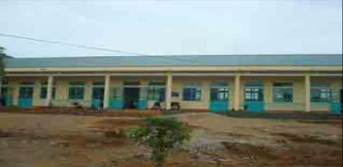 A single-story building with a light blue roof and blue doors. The building has multiple windows and is set in a sparsely vegetated area with bare ground in the foreground.