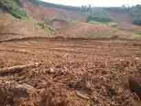 A cleared, muddy slope with scattered debris and exposed earth. Distant vegetation can be seen in the background.