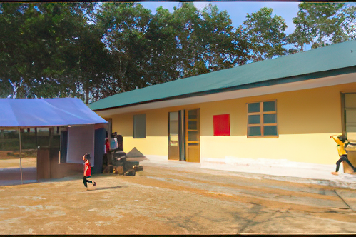 A child runs in front of a single-story yellow building with a green roof and a shaded outdoor area on a sunny day. Trees are visible in the background.