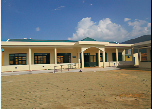 Single-story yellow building with green accents, flat terrain in the foreground, and blue sky with scattered clouds in the background.