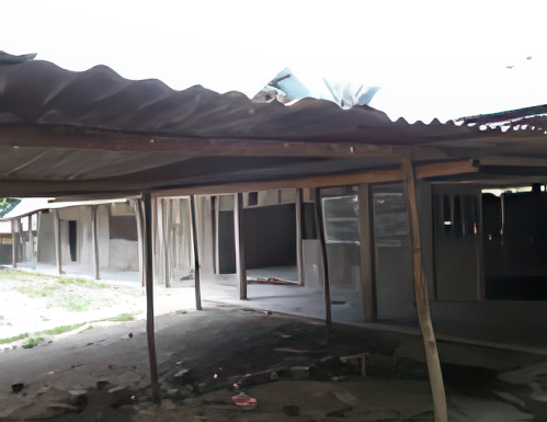 A dilapidated building with corrugated metal roofing and wooden supports. The structure appears abandoned and some areas are collapsing. Vegetation is sparse around the building.