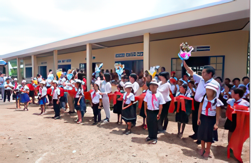 A group of schoolchildren and teachers, some holding gifts and others wearing hats, stand in lines outside a building with a sign in a non-Latin script.