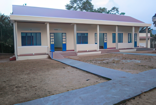 A single-story building with a maroon roof and beige walls, featuring blue doors and windows, is surrounded by a dirt yard and concrete pathways.