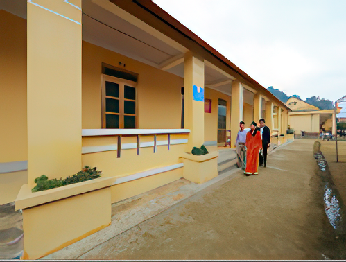 A long, beige building with a front walkway and several windows. Three people dressed in traditional clothing walk along the pathway on the right side.