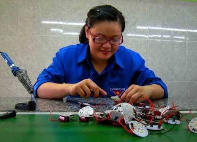 A person in glasses and a blue shirt works on assembling electronic components at a table with tools.